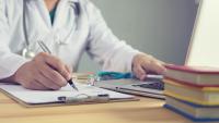 doctor hand holding silver pen writing something on clipboard closeup