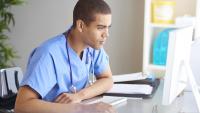 medical student in scrubs sitting at computer screen