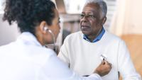 A enior adult man is at a routine medical appointment. He is seated facing his female doctor.